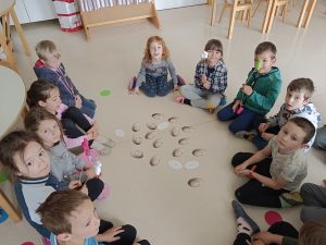 Učenci OPB sedijo na tleh učilnice v krogu - igrica s pirhi.