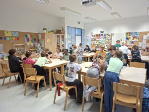Učenci 5. a razreda sedijo za mizami in sodelujejo pri dejavnostih v učilnici.